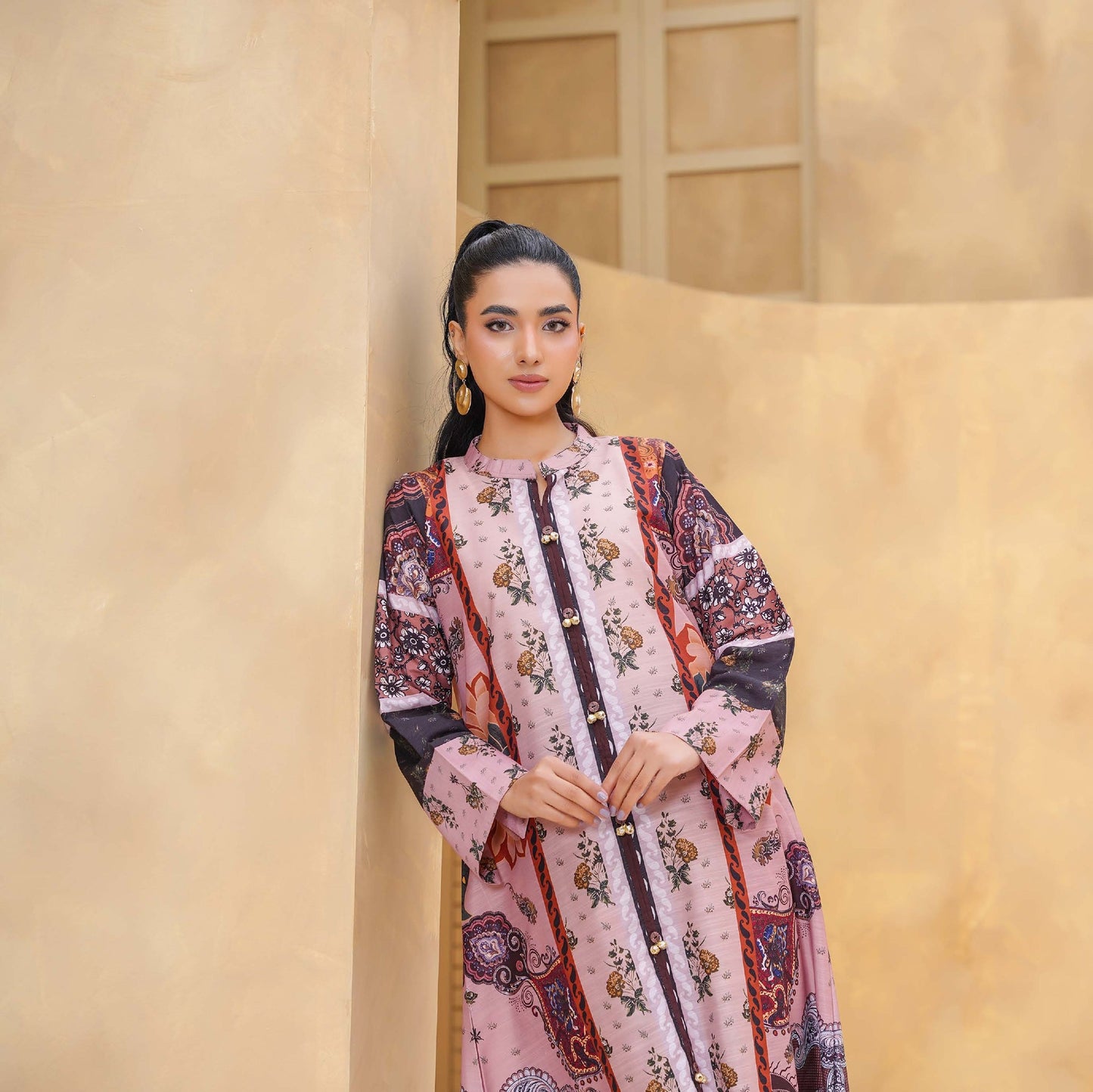 Woman in a floral dress standing against a beige wall with a plant in the background